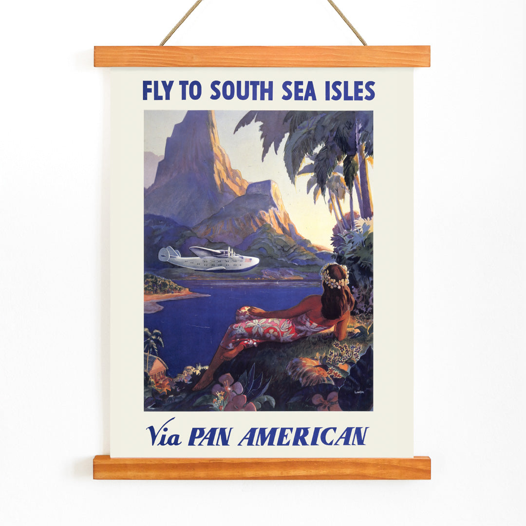 Vintage travel poster of a woman in a floral dress on a tropical island with a Pan American seaplane by Paul George Lawler, with wooden magnetic frame on white background