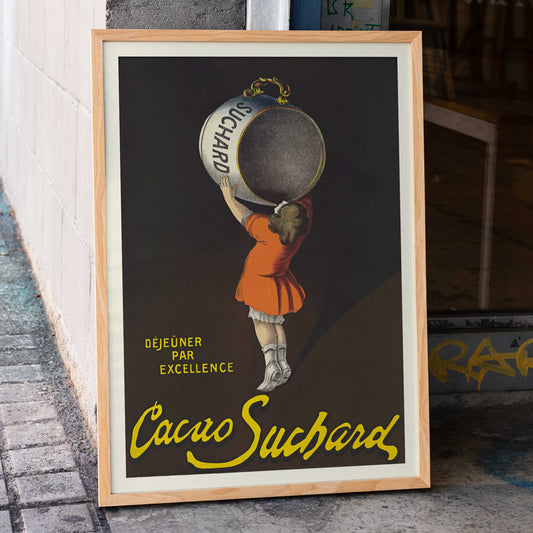 Leonetto Cappiello Cacao Suchard poster with girl lifting giant cocoa tin on dark background in orange dress and yellow lettering, framed and displayed in home decor