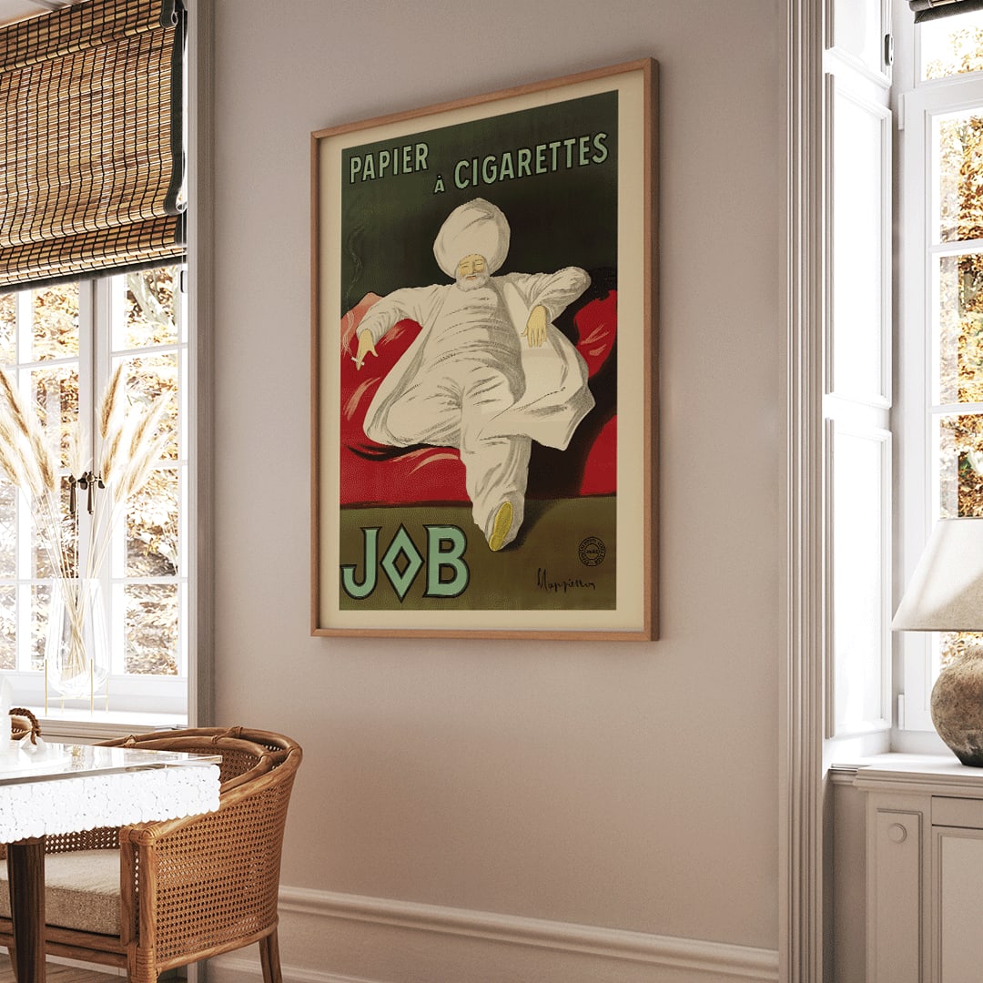 Cigarette Rolling Paper Job poster by Leonetto Cappiello showing a relaxed man in white robes and turban reclining with a cigarette on a red couch, framed and displayed in home decor