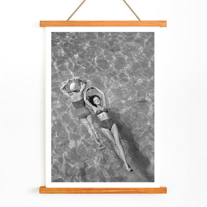 Fashion models in vintage bathing suits floating in a swimming pool artwork by Toni Frissell, with wooden magnetic frame on white background