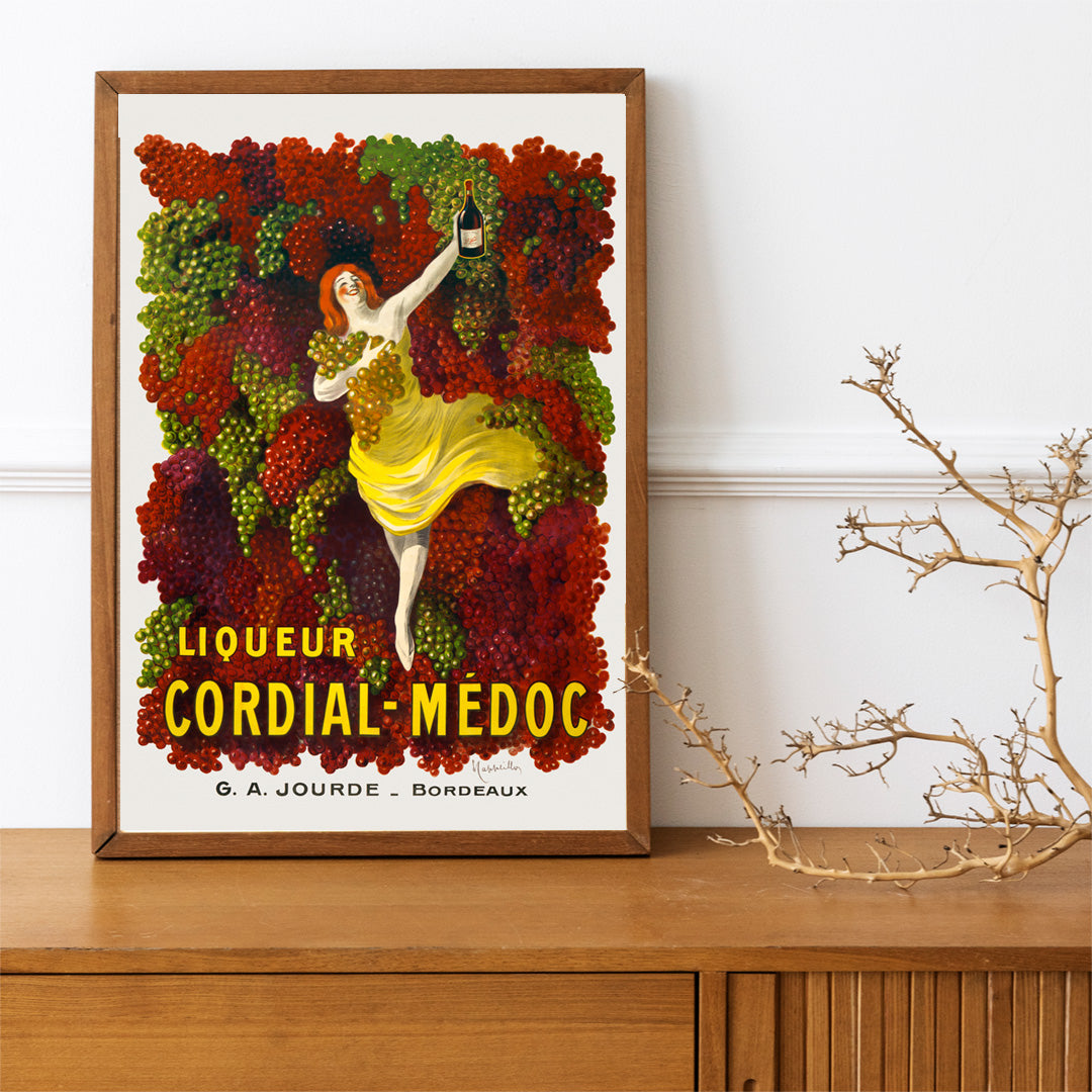 Liquor Cordial-Médoc poster by Leonetto Cappiello showing a woman in a yellow dress surrounded by colorful grapes holding a bottle, framed and displayed in home decor